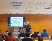 Ponente presentando las jornadas sobre el azud de Riolobos ante un público en una sala de conferencias, con una diapositiva de mapa proyectada en pantalla.