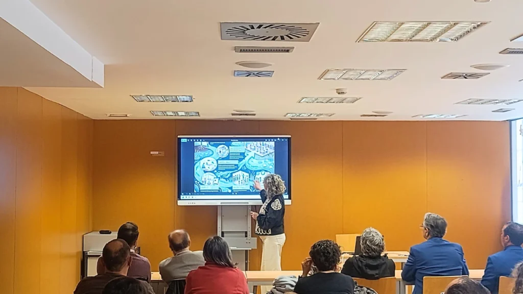 Ponente presentando las jornadas sobre el azud de Riolobos ante un público en una sala de conferencias, con una diapositiva de mapa proyectada en pantalla.