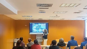 Ponente presentando las jornadas sobre el azud de Riolobos ante un público en una sala de conferencias, con una diapositiva de mapa proyectada en pantalla.