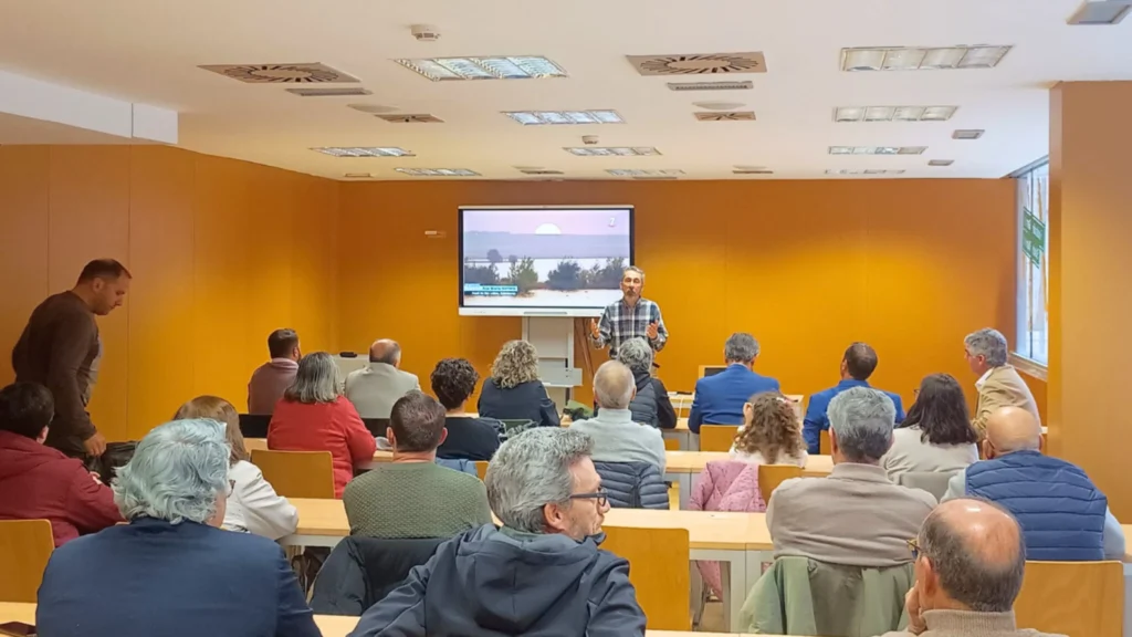 Ponente presentando las jornadas sobre el azud de Riolobos ante un público en una sala de conferencias, con una diapositiva de mapa proyectada en pantalla.